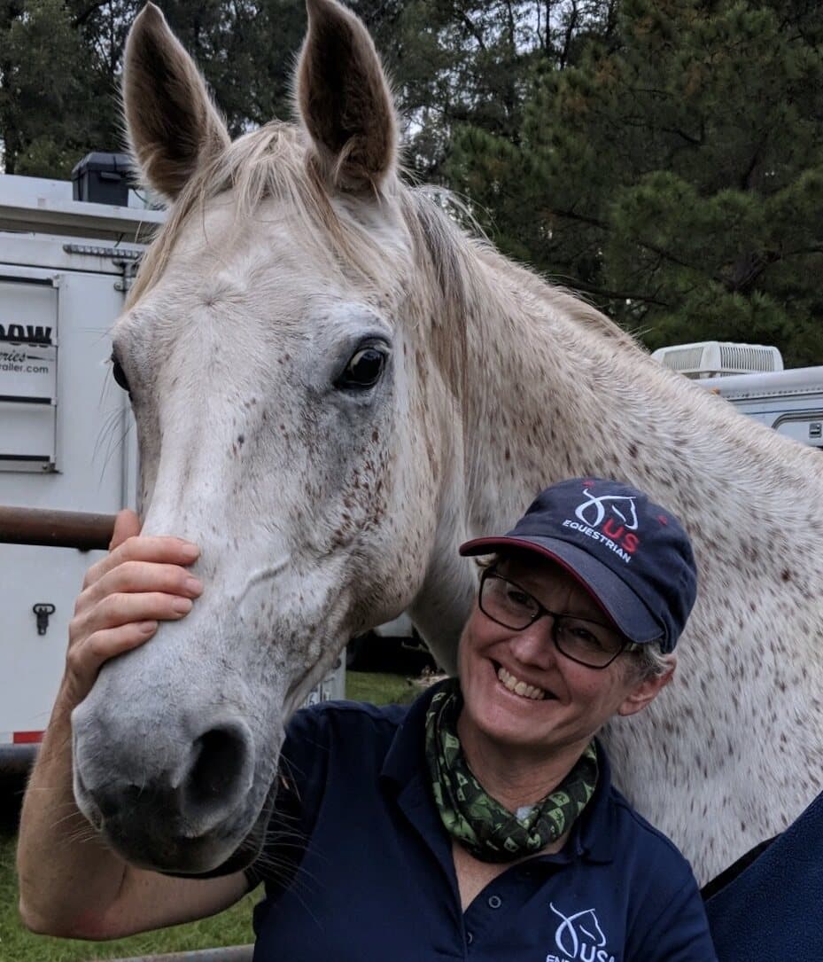 Holly Corcoran smiling beside her gray horse, Poetrie.